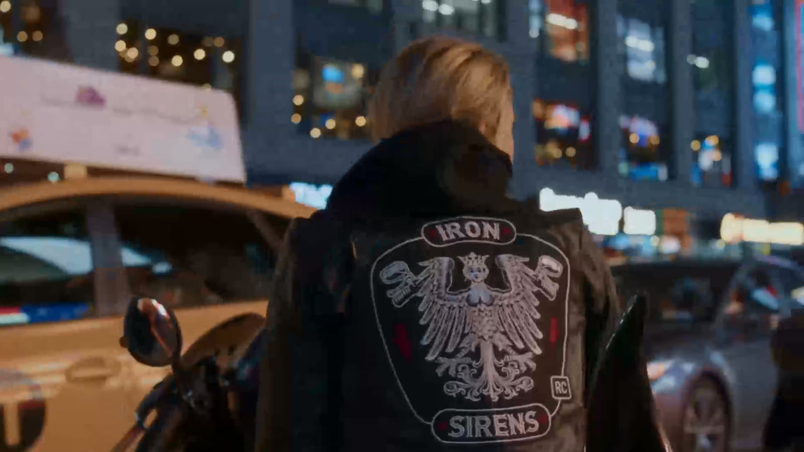 A Siren walking through Times Square at night, the embroidered IRON SIRENS colors on the back of her kutte.